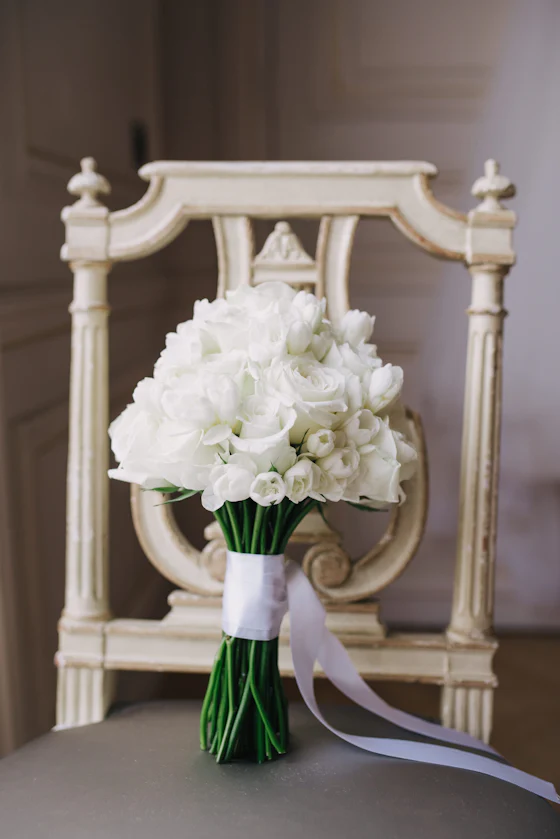 A tied bouquet of white blooms resting on a carved white chair.