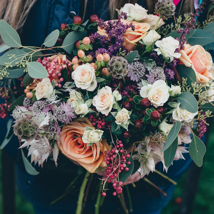 A dense bouquet of roses, berries and wildflowers in rich pinks and oranges.