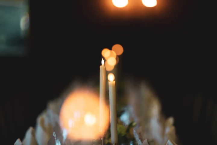 Two tapers burning on a dark table, their light softening into golden bokeh.