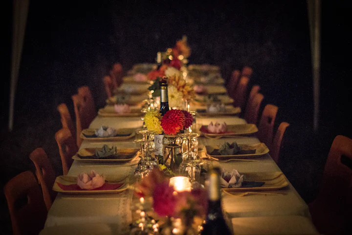 A long candlelit table with deep red and yellow flowers running down its length.