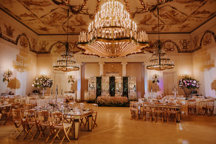 A grand ballroom with a large crystal chandelier over set dining tables.