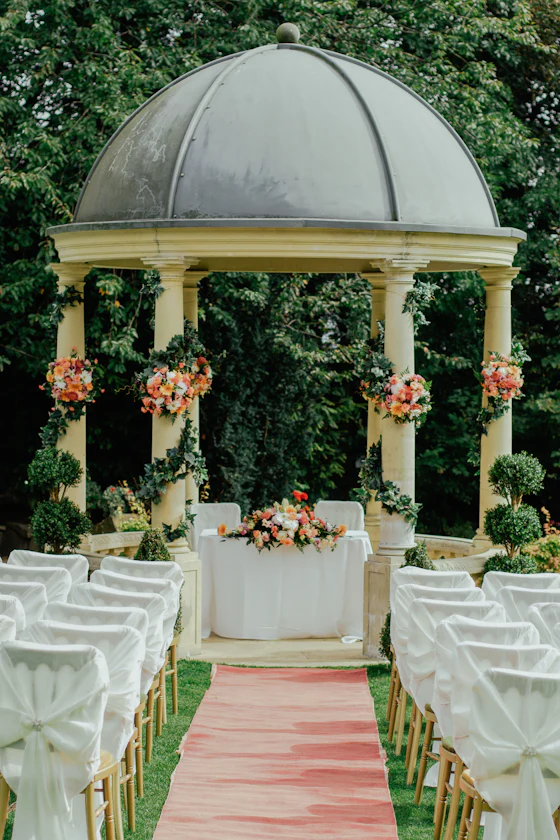 A domed white gazebo at the end of a rose-petal aisle between white chairs.