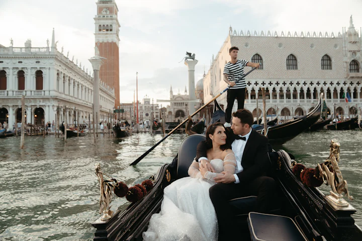 A bride and groom seated in a gondola on a Venetian canal.