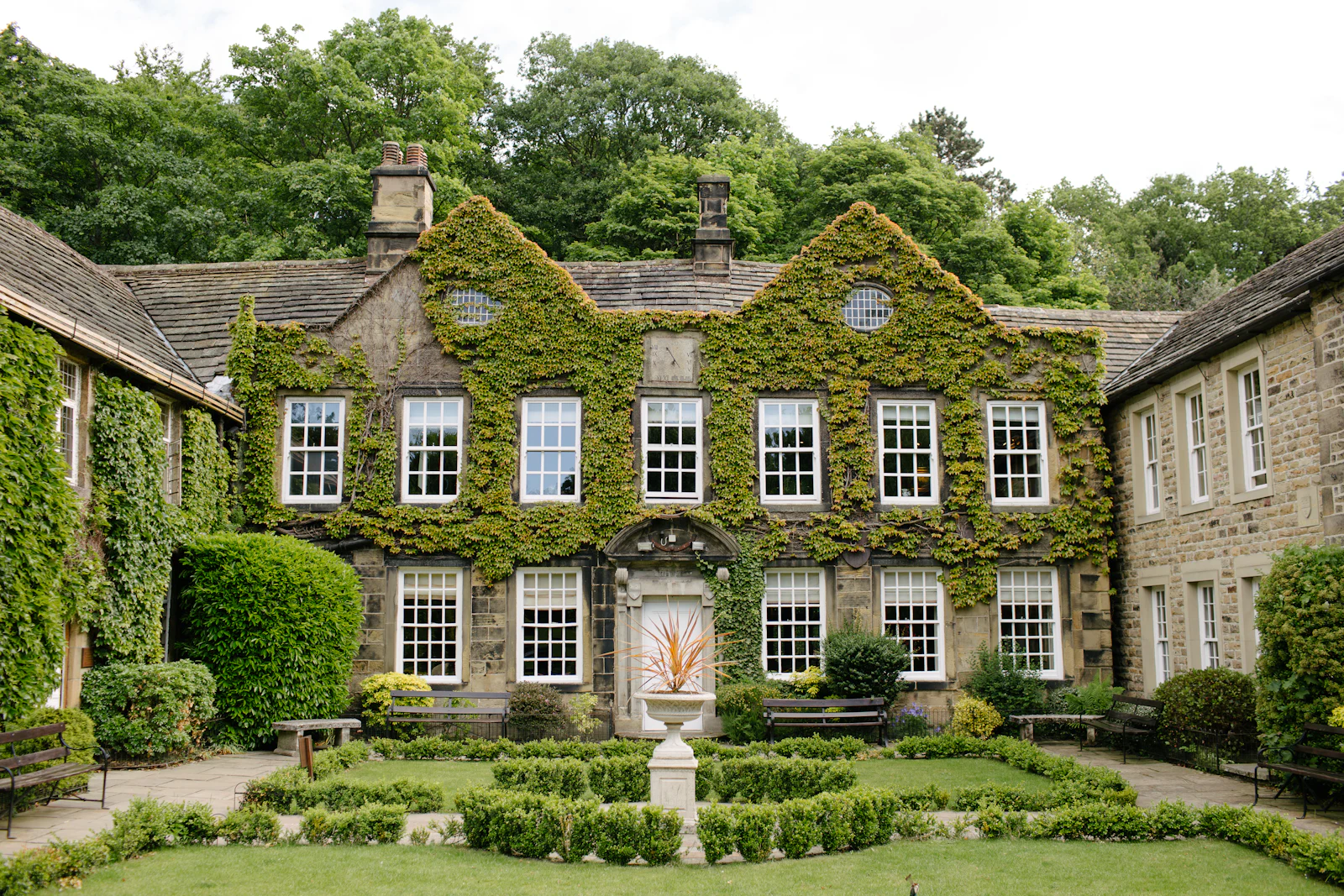 An ivy-covered manor house with tall white-framed windows, seen from its formal garden.