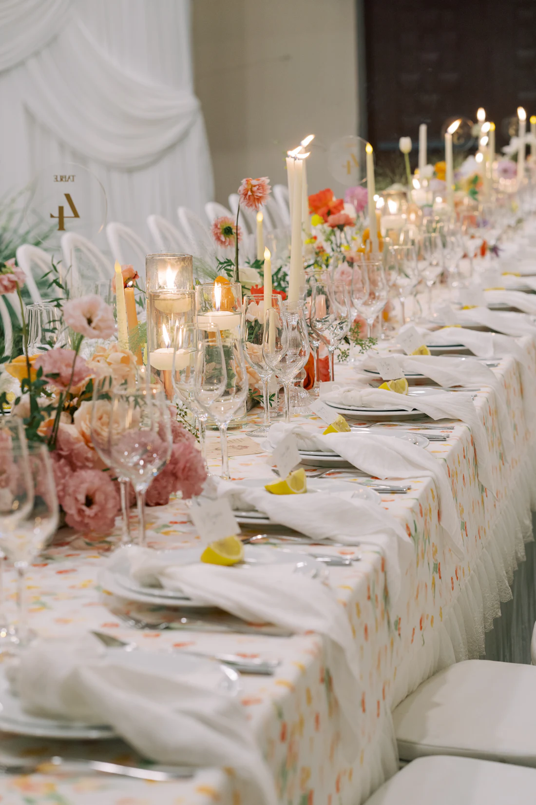 A long banquet table dressed with blush garden roses, taper candles and linen, laid before guests arrive.