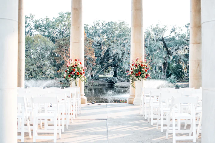 A white columned pavilion beside still water, framed by a wide old oak tree.