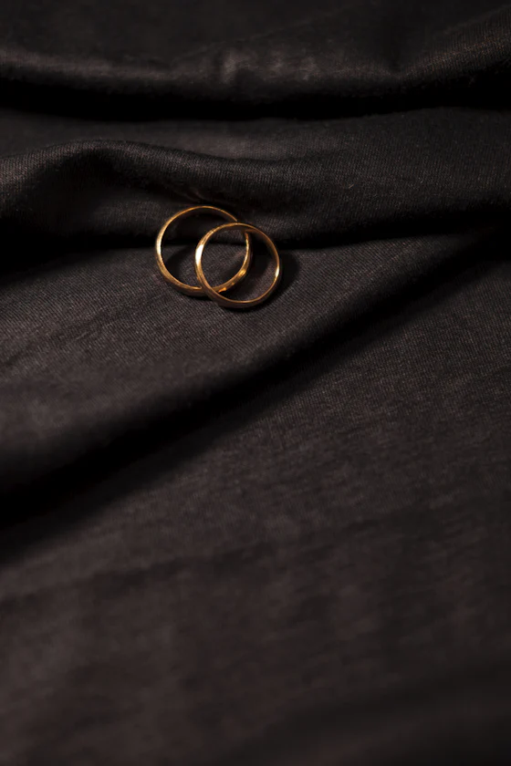 Two gold wedding bands resting on dark folded fabric.