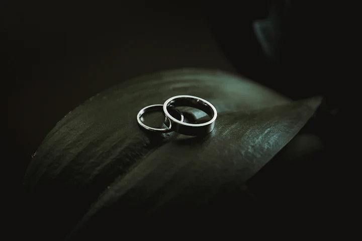 Two silver wedding bands resting on a dark green surface.