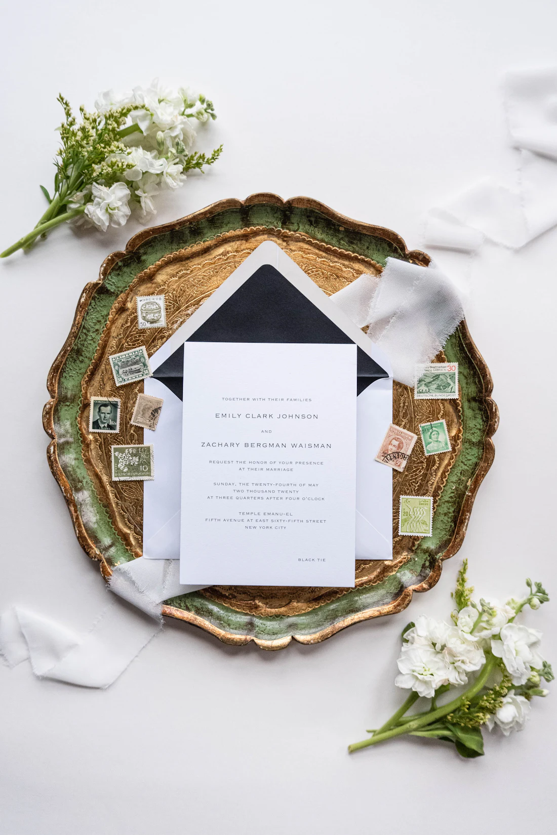 Letterpress stationery with a black envelope and postage stamps laid on a green and gold plate.