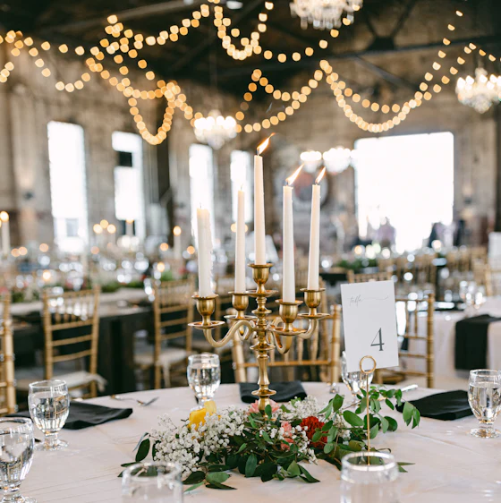 A table set with a brass candelabra beneath looping string lights.