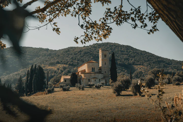 A stone chapel on a golden hillside among cypress trees.