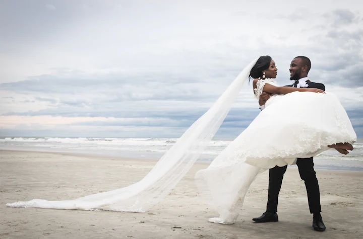 A long bridal veil drifting across pale sand beside the sea.