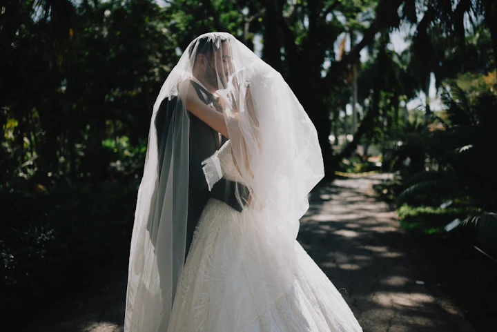 A couple embracing beneath a long veil in the shade of old oak trees.