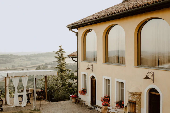 A pale villa with arched windows and a terrace, red geraniums at the door.